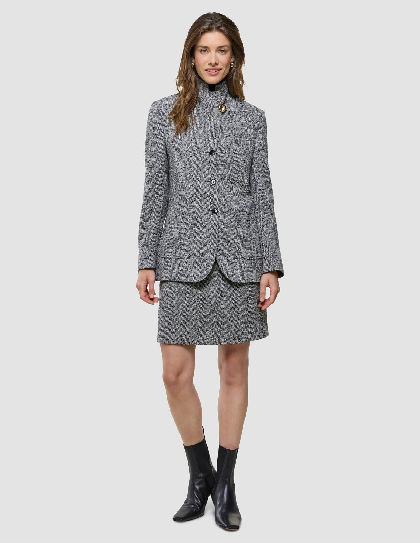 En kvinna bär en grå blazer med svartvitt fiskbensmönster tillsammans med en matchande kort kjol från Women Ashryn och svarta ankelstövlar.